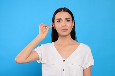 Photo of Young woman cleaning ear with cotton swab on light blue background