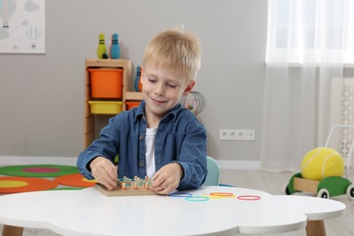 Motor skills development. Boy playing with geoboard and rubber bands at white table in room