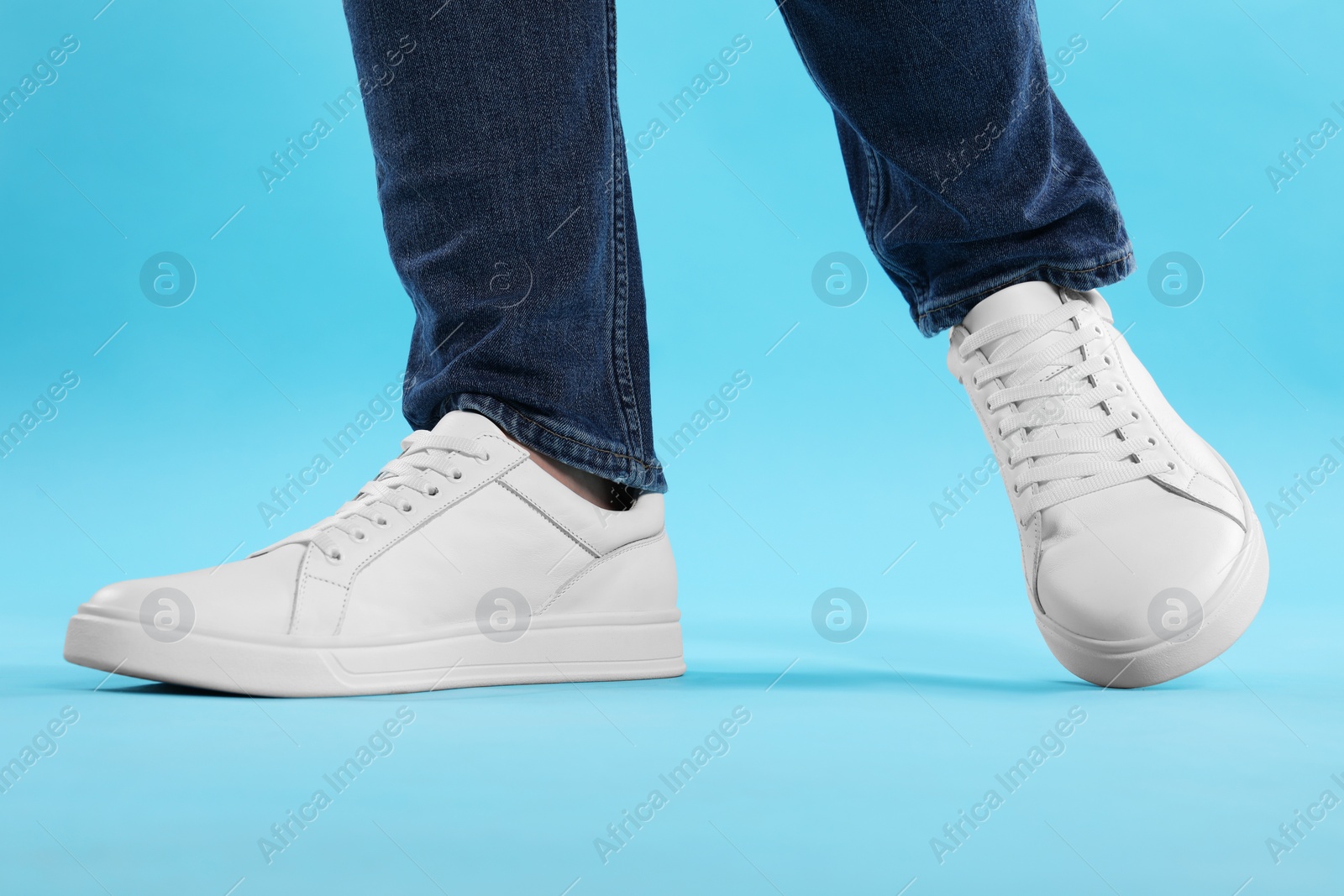 Photo of Man wearing stylish white sneakers on light blue background, closeup