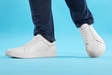 Photo of Man wearing stylish white sneakers on light blue background, closeup