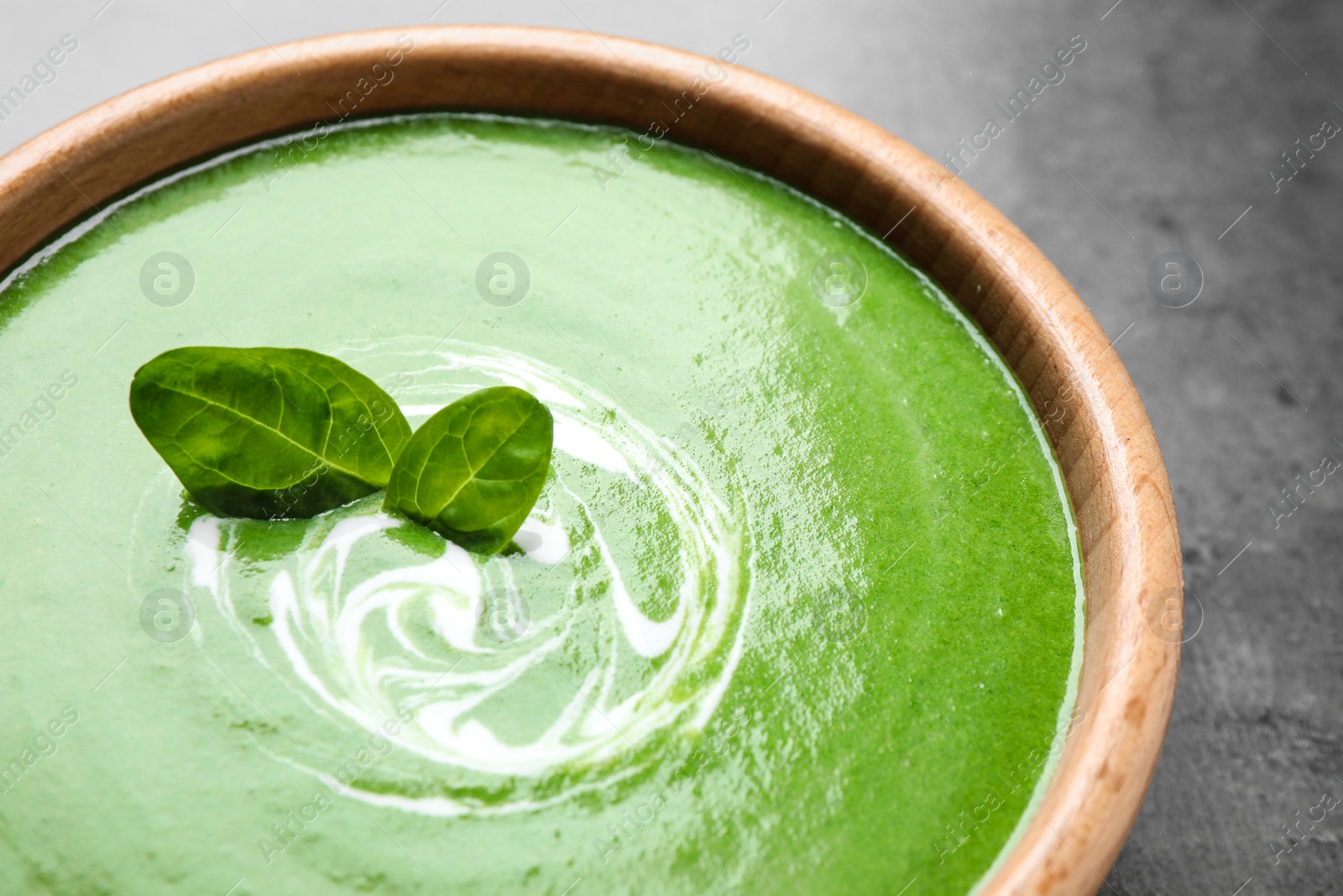 Photo of Bowl of healthy green soup with fresh spinach on grey table, closeup view