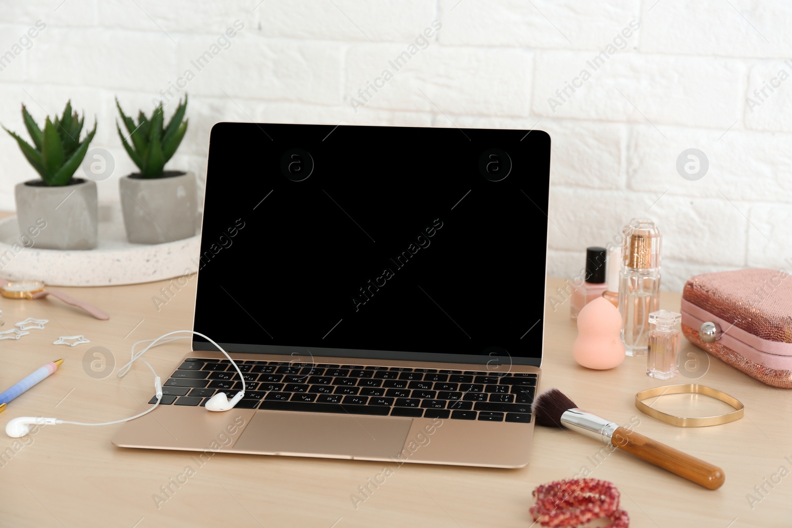 Photo of Stylish workplace with modern laptop and cosmetic products on table near brick wall. Beauty blogger