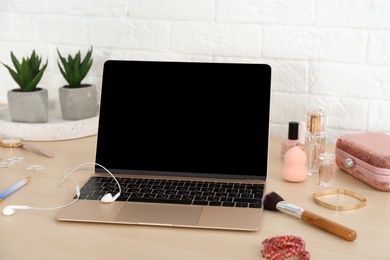 Stylish workplace with modern laptop and cosmetic products on table near brick wall. Beauty blogger