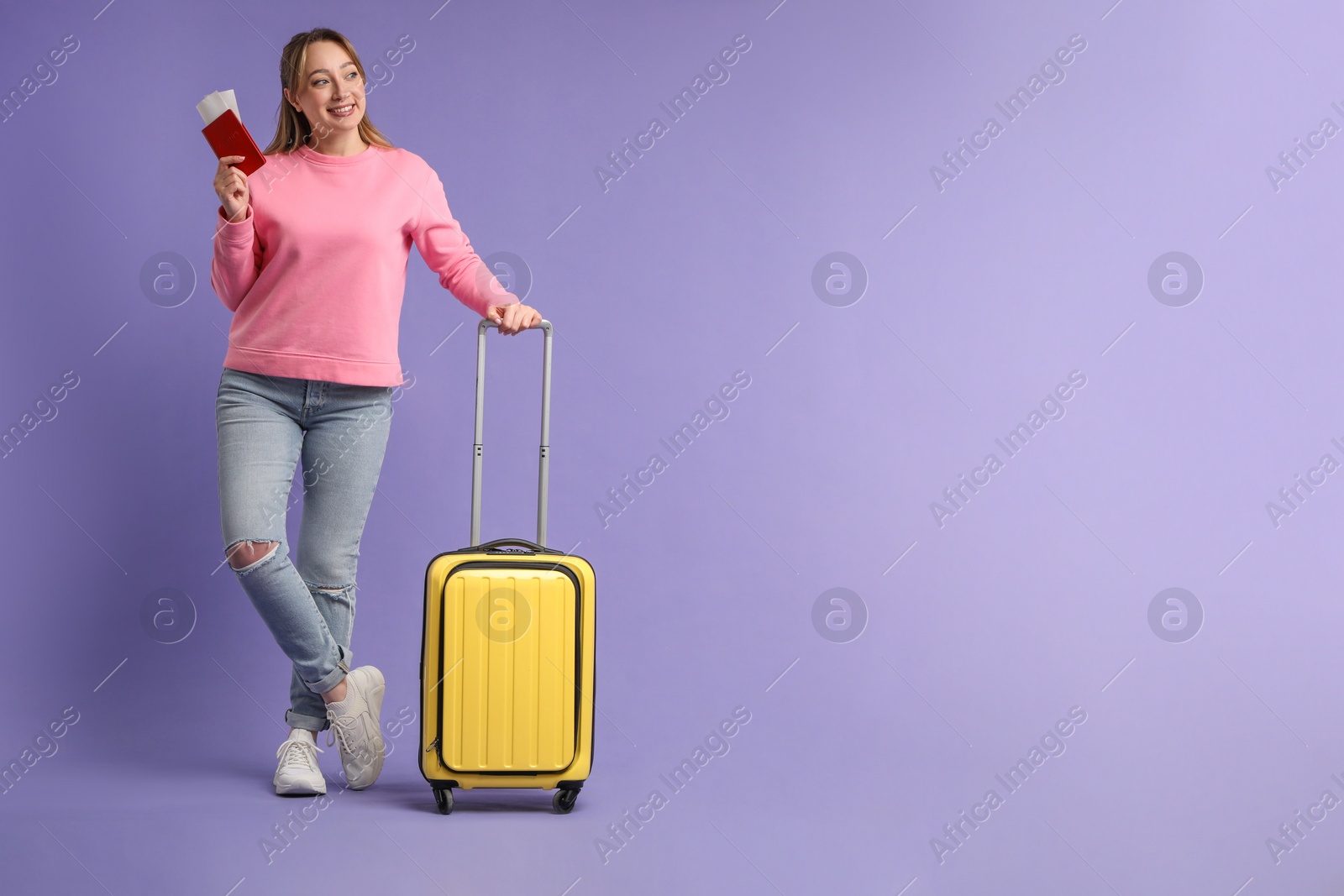 Photo of Happy young woman with passport, ticket and suitcase on purple background, space for text