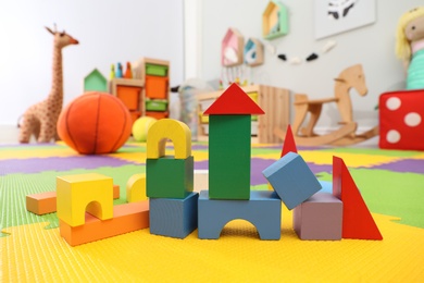 Wooden castle made of colorful blocks on carpet in playroom. Interior design