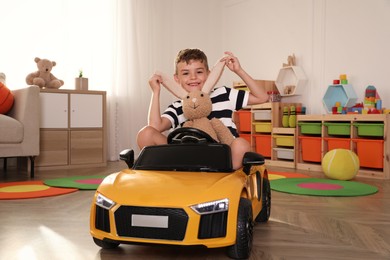 Photo of Cute little boy playing with stuffed bunny and big toy car at home