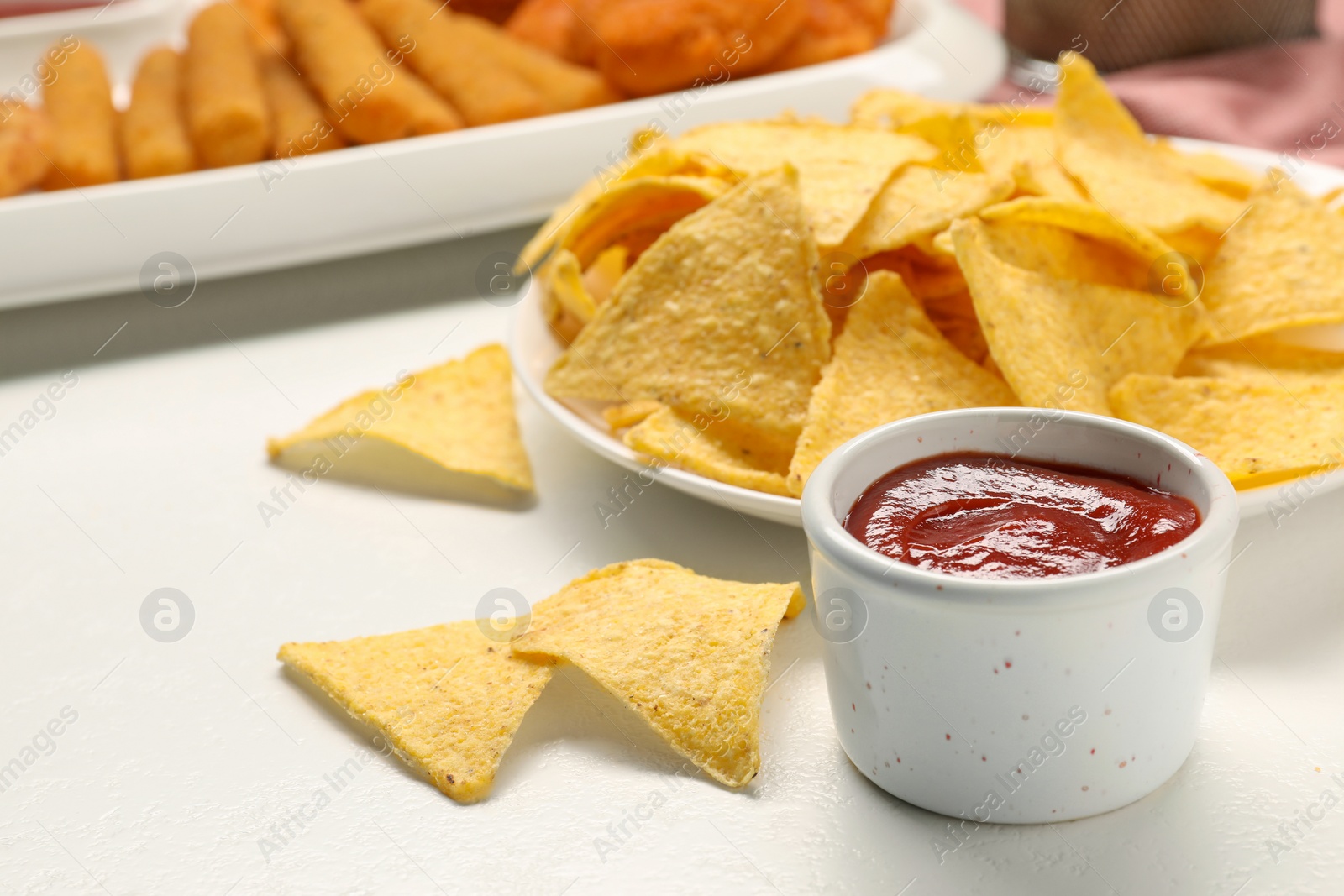 Photo of Tasty ketchup and tortilla chips on white table, closeup