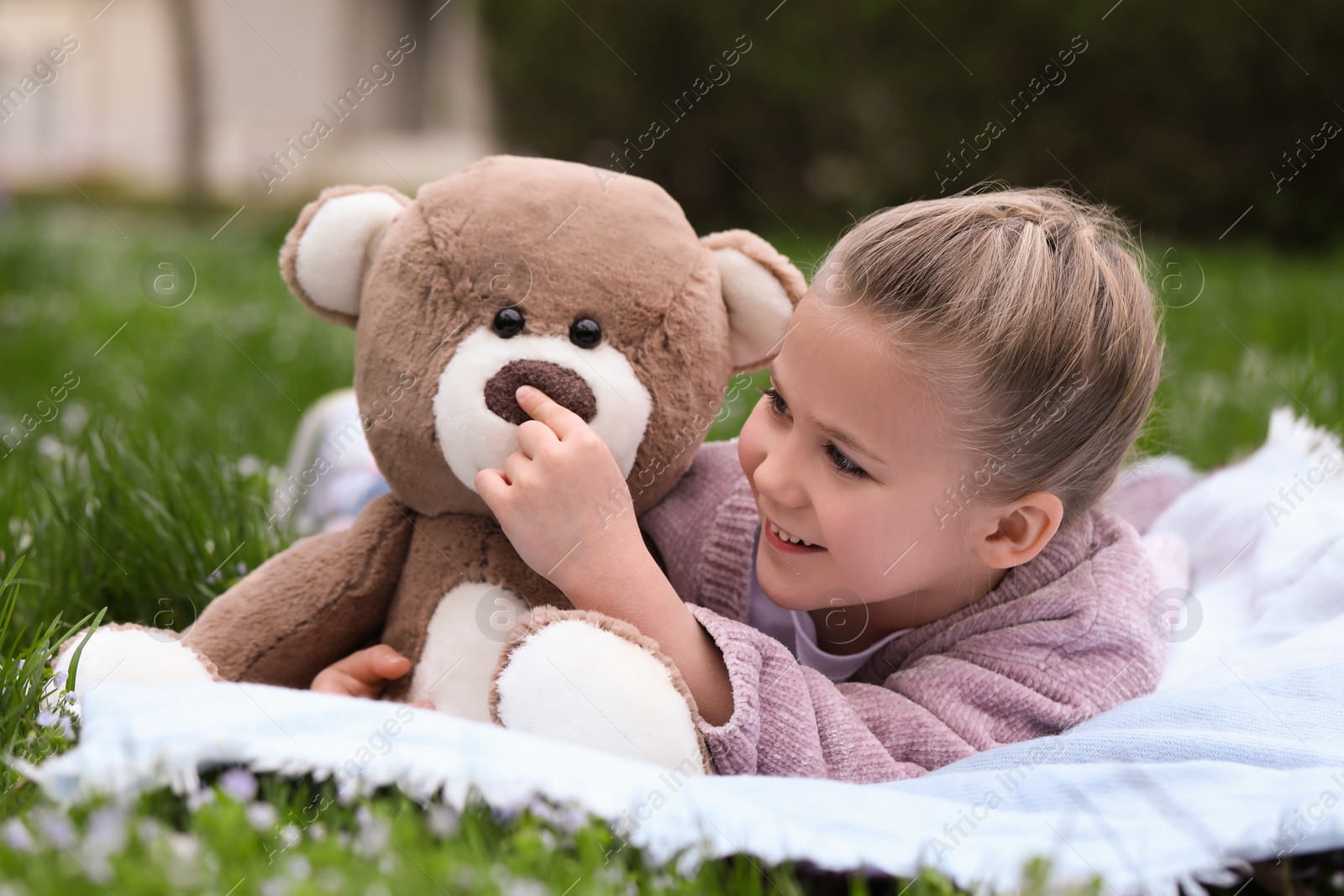 Photo of Little girl with teddy bear on plaid outdoors