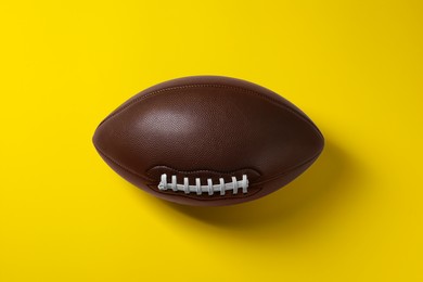 Photo of American football ball on yellow background, above view.