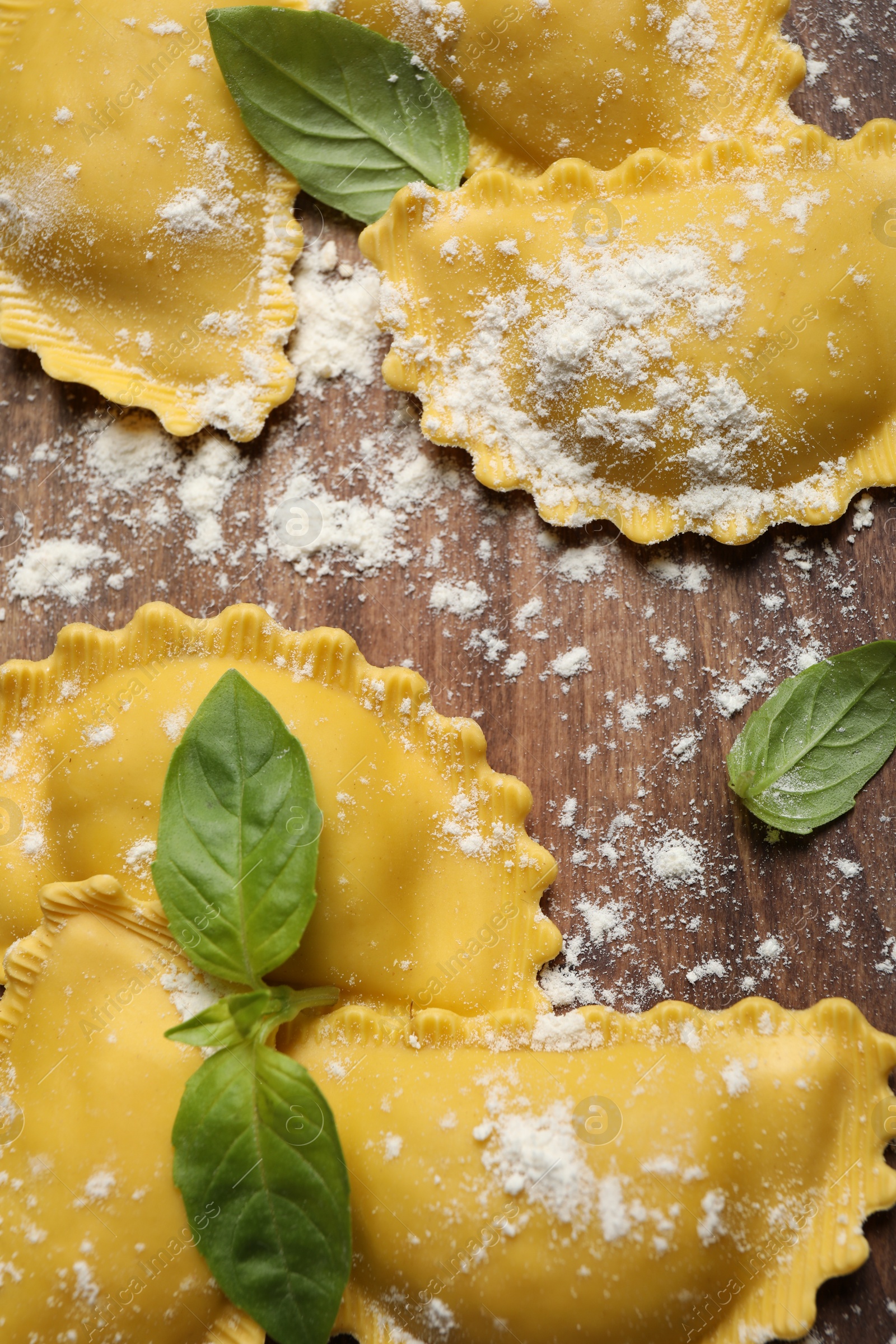 Photo of Raw ravioli with basil on wooden table, flat lay. Italian pasta