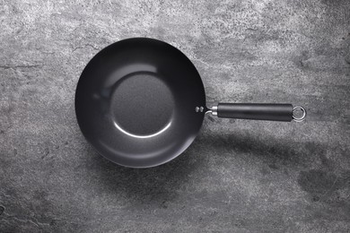 Photo of Empty iron wok on grey textured table, top view. Chinese cookware