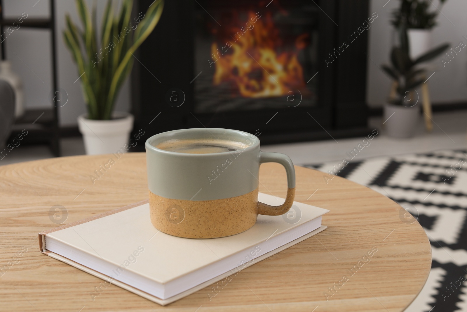 Photo of Cup with hot coffee and book on wooden table indoors