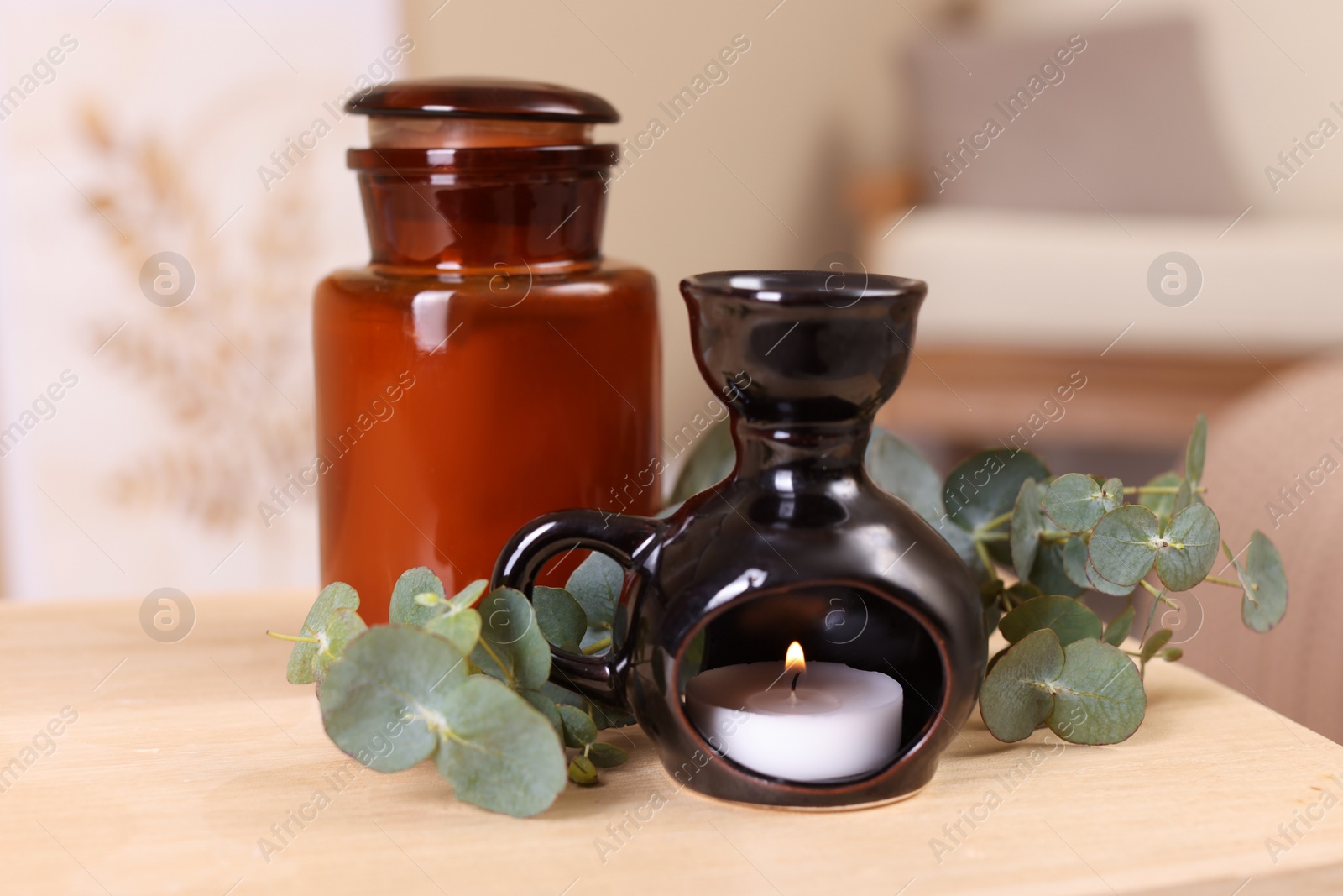 Photo of Stylish aroma lamp, candle and eucalyptus branches on wooden table indoors