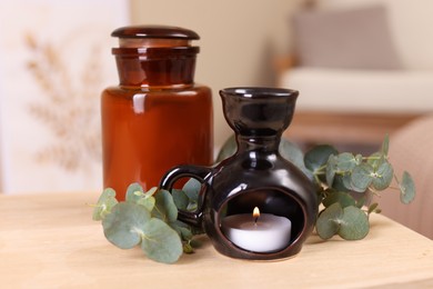 Stylish aroma lamp, candle and eucalyptus branches on wooden table indoors