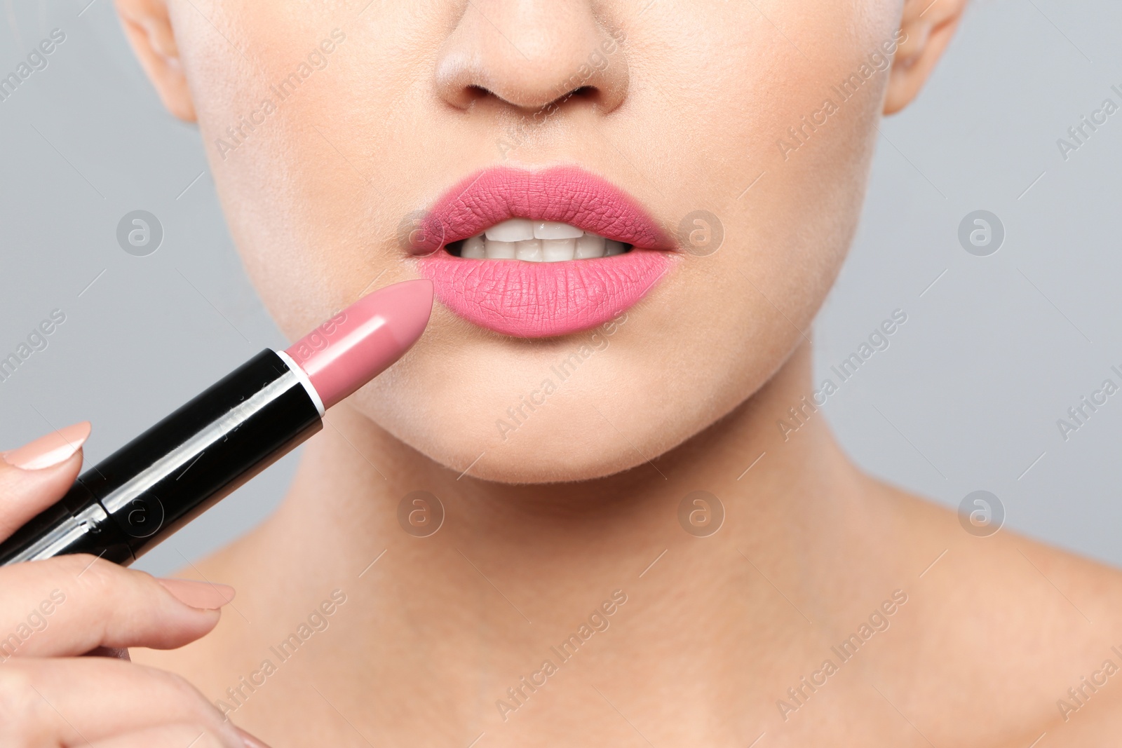 Photo of Young woman applying beautiful lipstick on gray background, closeup