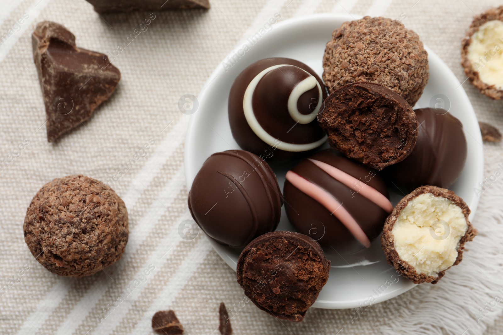 Photo of Many different delicious chocolate truffles on kitchen towel, flat lay