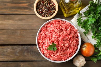 Raw ground meat in bowl, spices, oil and parsley on wooden table, flat lay. Space for text