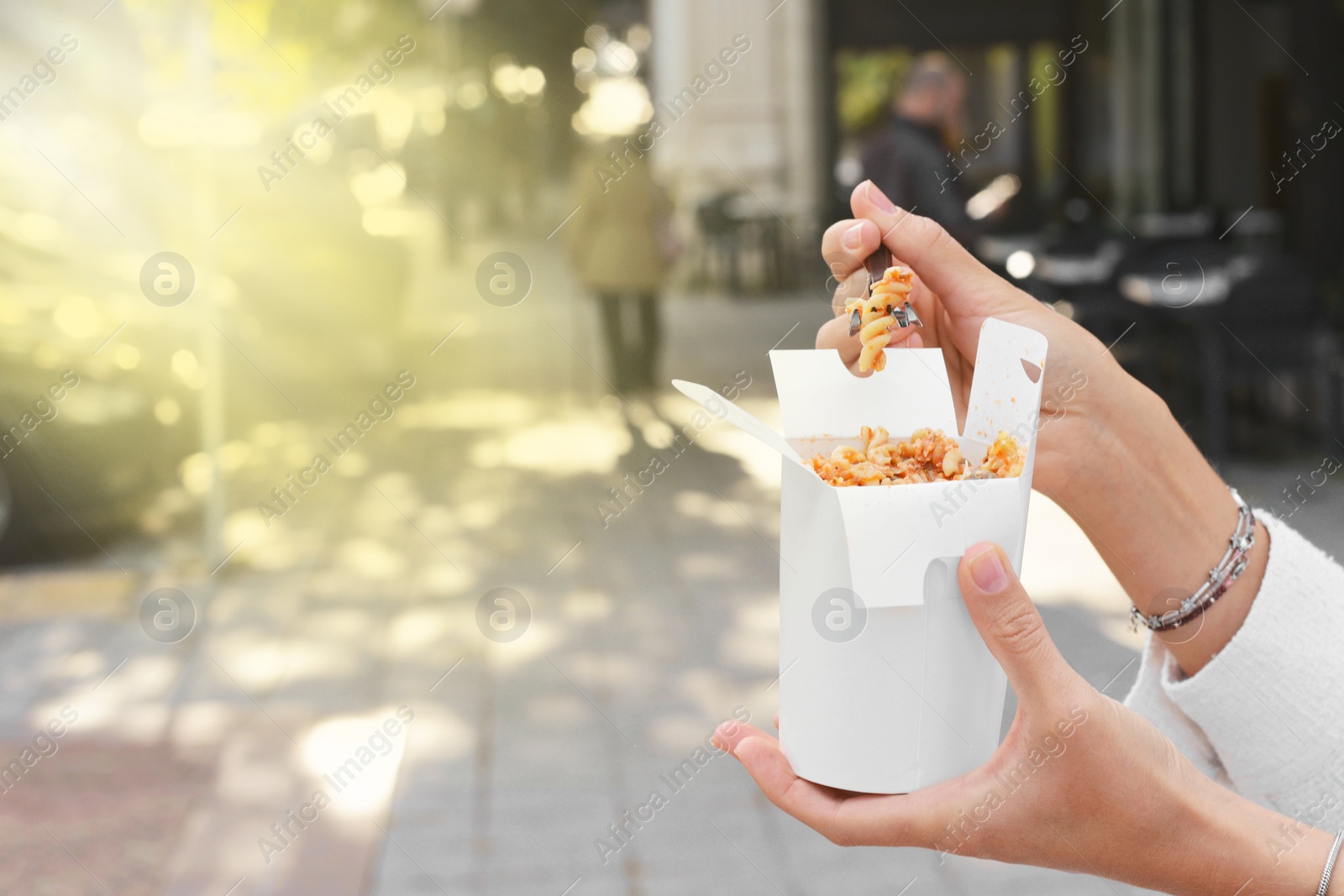 Photo of Woman eating takeaway noodles from paper box with fork outdoors, closeup and space for text. Street food