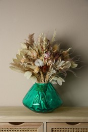 Photo of Beautiful dried flower bouquet in glass vase on wooden table near light grey wall