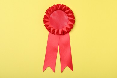 Photo of Red award ribbon on yellow background, top view