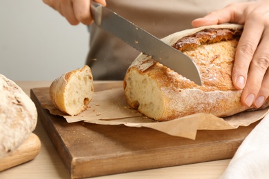 Photo of Woman cutting freshly baked bread at wooden table, closeup