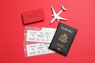 Flight tickets, passport, plane model and SALE card on red background, flat lay