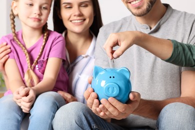 Photo of Happy family putting coin into piggy bank, closeup