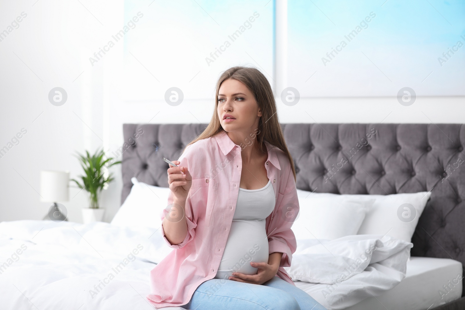 Photo of Young pregnant woman smoking cigarette in bedroom. Harm to unborn baby