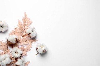 Fluffy cotton flowers and decorative leaf on white background, flat lay. Space for text