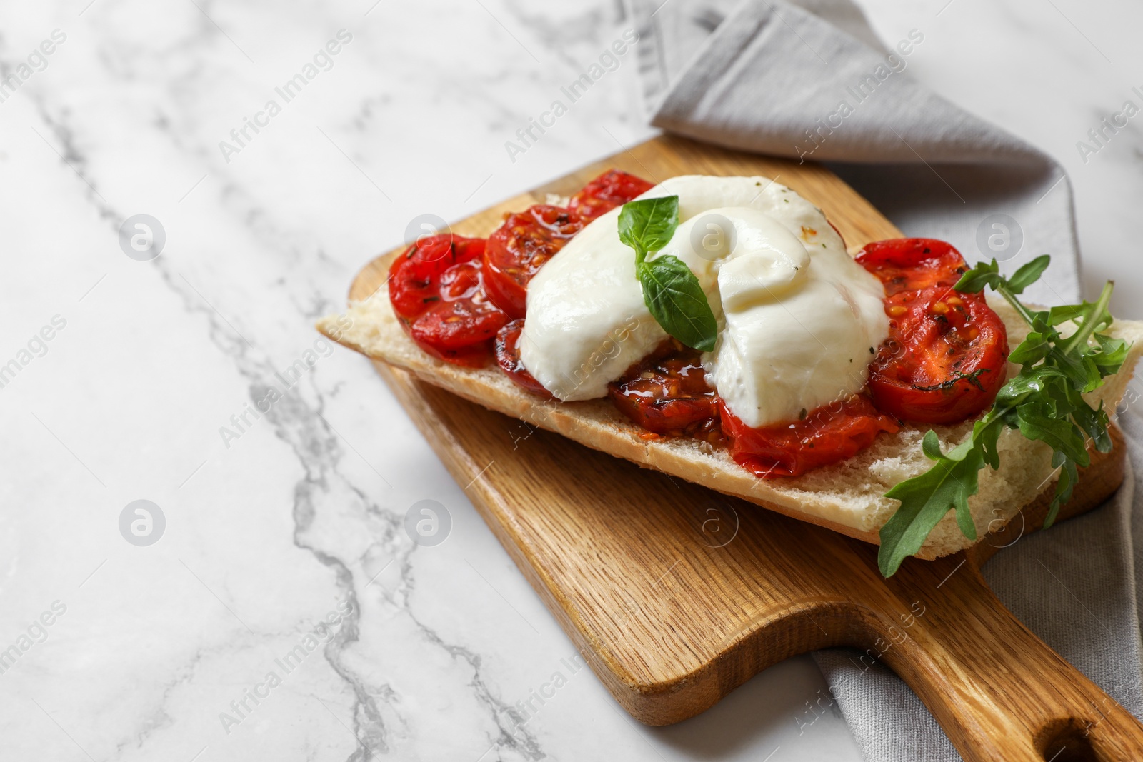 Photo of Toast with delicious burrata cheese, tomatoes and arugula on white marble table, space for text