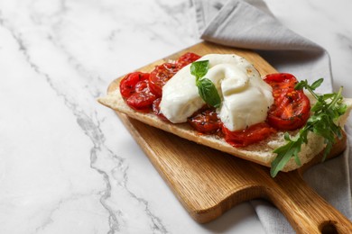 Photo of Toast with delicious burrata cheese, tomatoes and arugula on white marble table, space for text