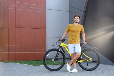 Photo of Handsome young man with bicycle on city street. Space for text