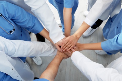 Team of medical workers holding hands together indoors, top view. Unity concept