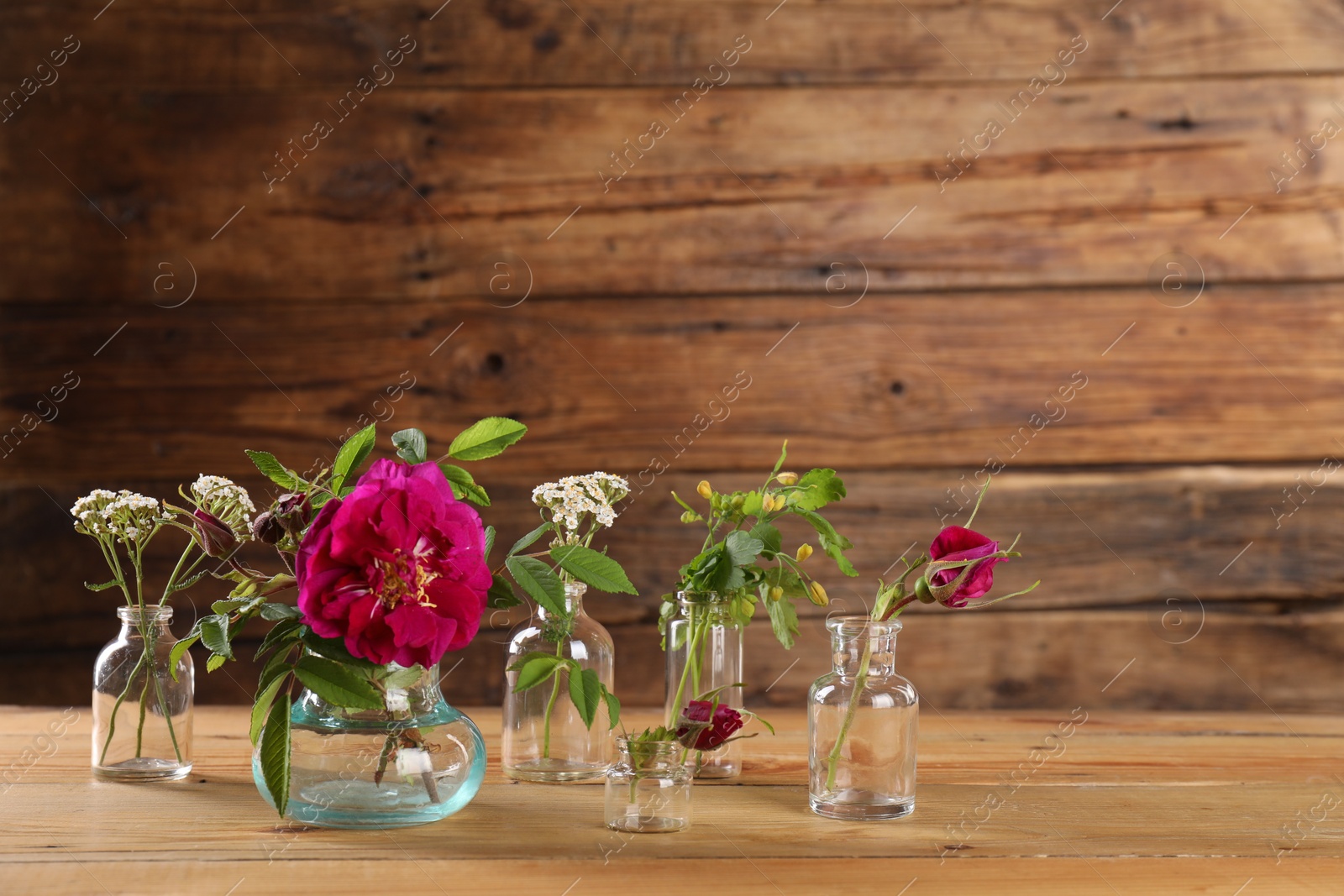 Photo of Different flowers in glass bottles on wooden table