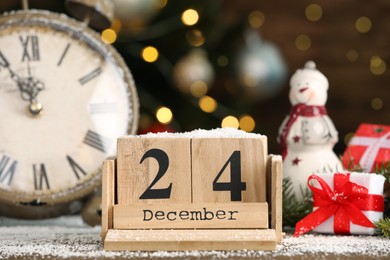 Photo of December 24 - Christmas Eve. Wooden block calendar, watch and festive decor on table against blurred lights