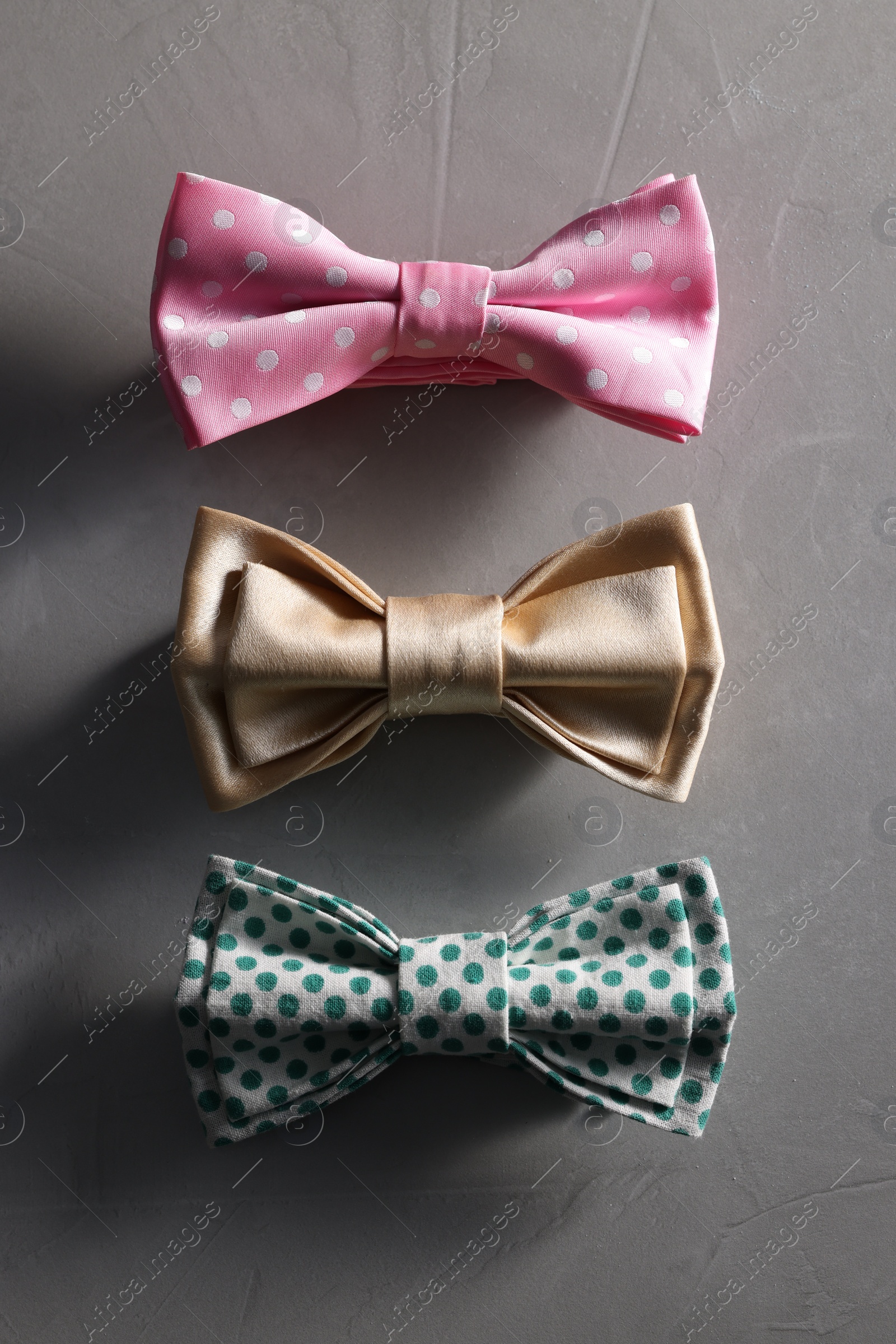 Photo of Stylish color bow ties on gray textured background, flat lay
