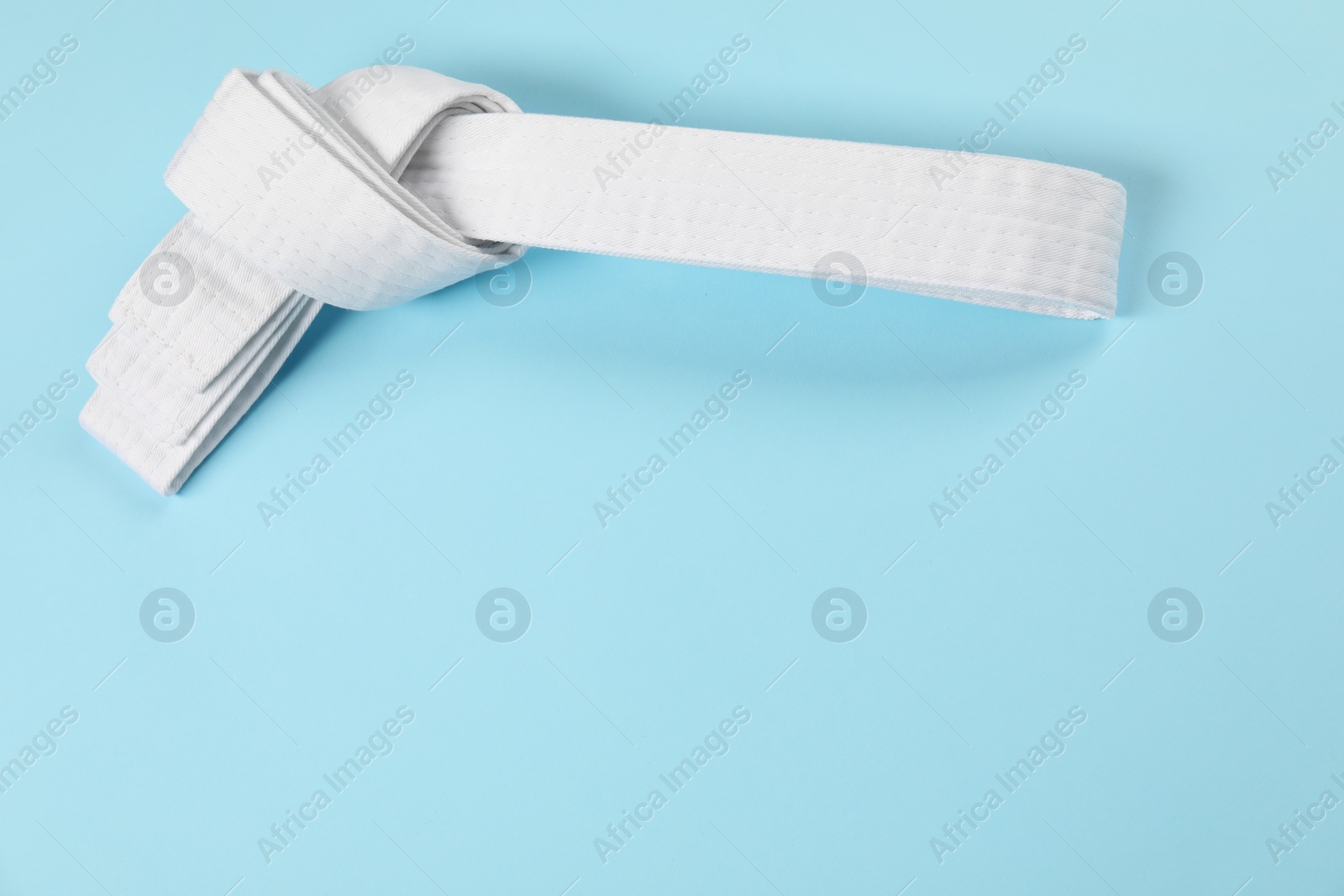 Photo of White karate belt on light blue background, top view. Space for text