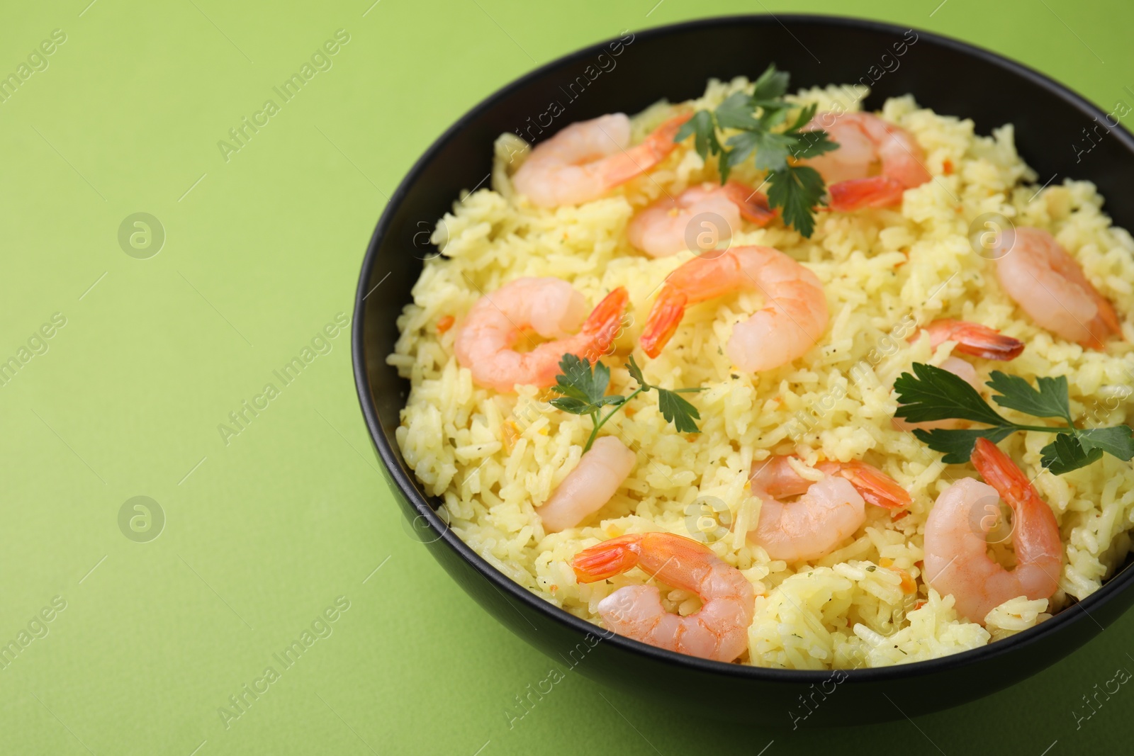 Photo of Delicious risotto with shrimps and parsley in bowl on light green background, closeup. Space for text