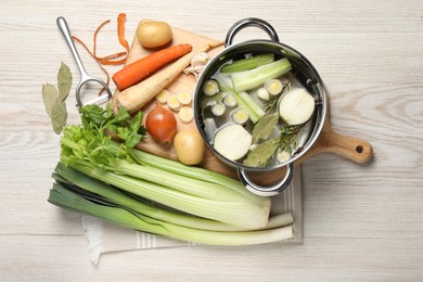 Pot and different ingredients for cooking tasty bouillon on white wooden table, flat lay