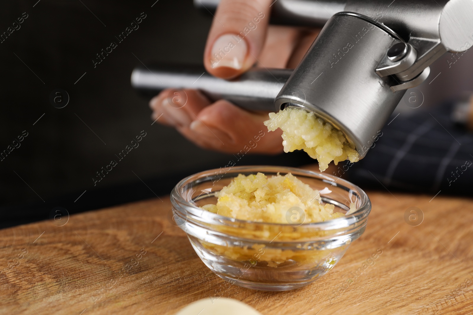 Photo of Woman squeezing garlic with press at wooden table, closeup