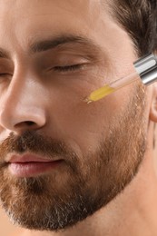Photo of Handsome man applying cosmetic serum onto his face, closeup