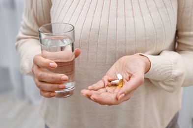 Woman with vitamin pills and glass of water indoors, closeup