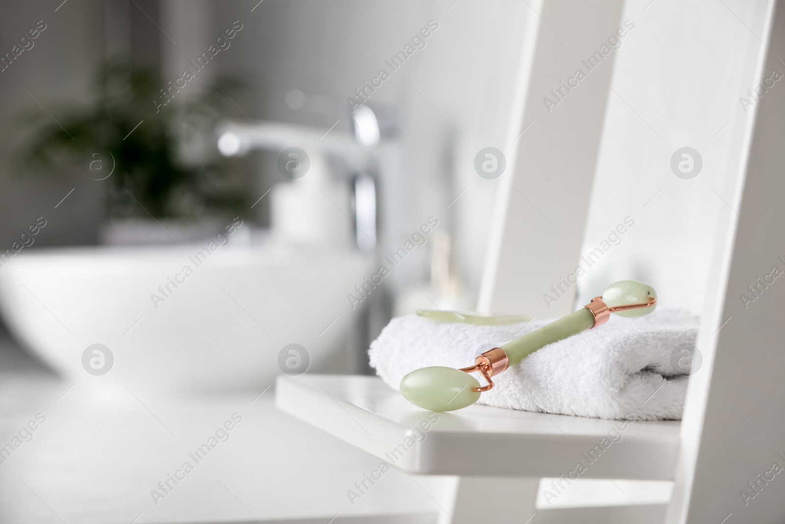 Photo of Natural face roller and towel on shelving unit in bathroom. Space for text