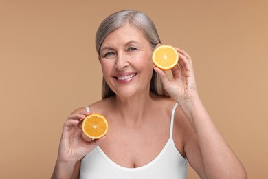 Beautiful woman with halves of orange rich in vitamin C on beige background