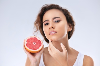 Photo of Beautiful young woman with acne problem holding grapefruit on light background. Skin allergy