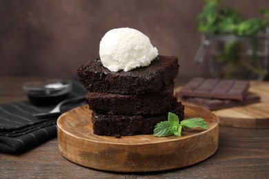 Photo of Tasty brownies served with ice cream on wooden table, closeup