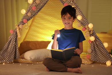 Photo of Preteen boy with flashlight reading book at home
