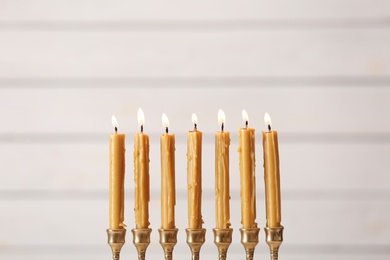 Photo of Golden menorah with burning candles on light background, space for text