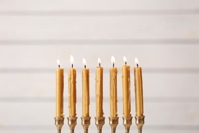 Golden menorah with burning candles on light background, space for text