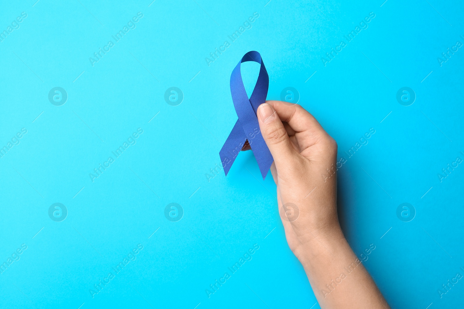 Photo of Woman holding blue awareness ribbon on color background, top view. Symbol of social and medical issues